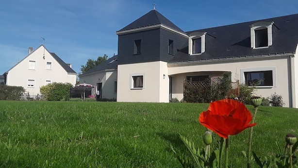 Una casa grande de dos pisos con un césped bien cuidado y una flor roja en primer plano.
