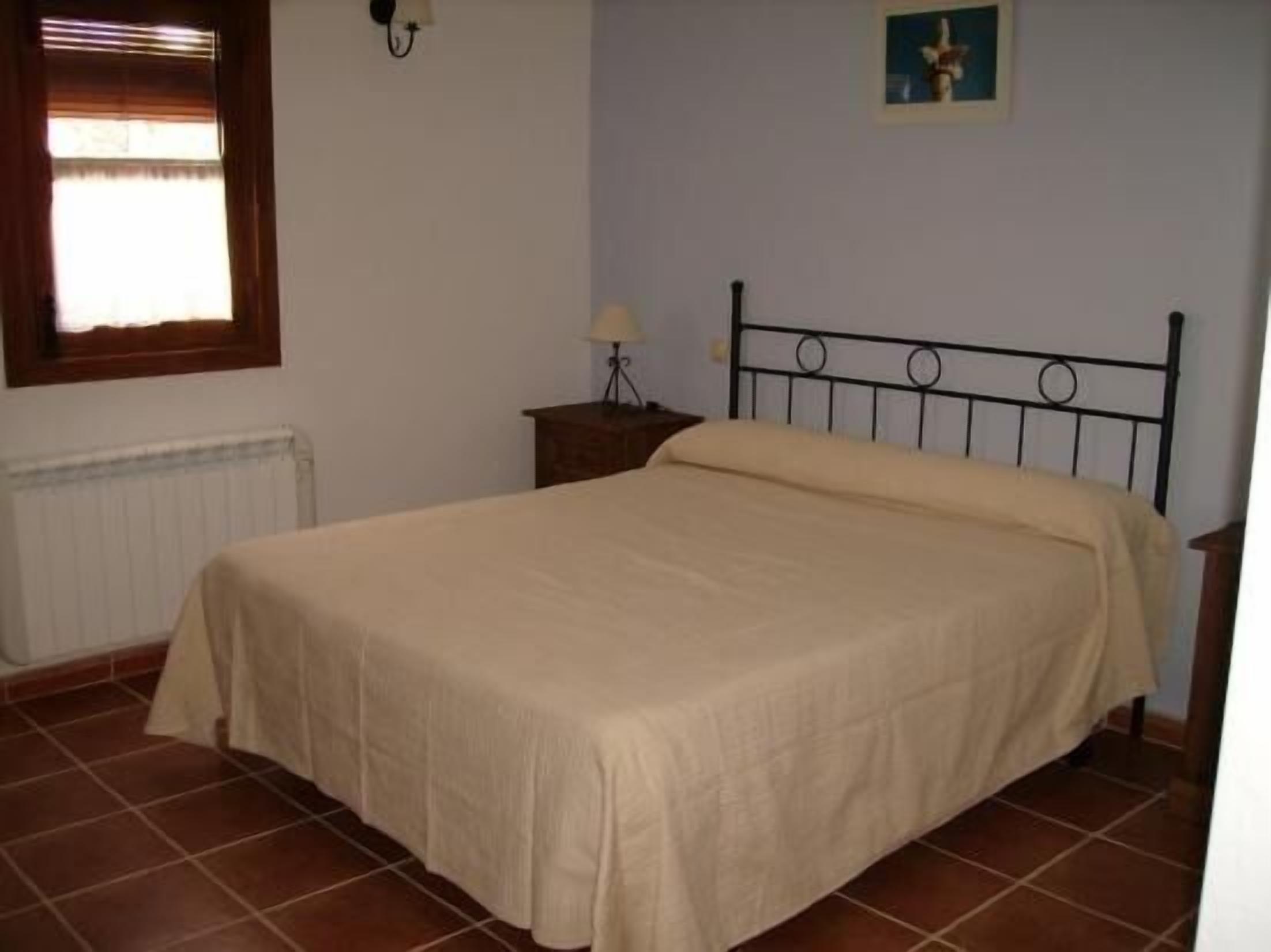 Ein Schlafzimmer mit Bett, Nachttisch, Lampe, Heizkörper und einem Fenster mit Jalousien.