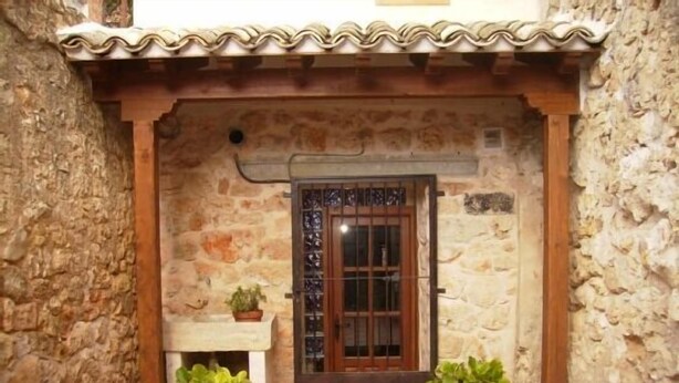 A stone building with a tiled roof, a wooden door with a metal gate, and potted plants at the entrance. - Rural house (full rental) El Empecinado for 23 people (Fuentelviejo)