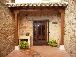 A stone building with a tiled roof, a wooden door with a metal gate, and potted plants at the entrance. - Rural house (full rental) El Empecinado for 23 people (Fuentelviejo)