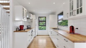 Una cocina moderna con armarios blancos, encimeras de madera y vistas a la vegetación a través de una ventana.