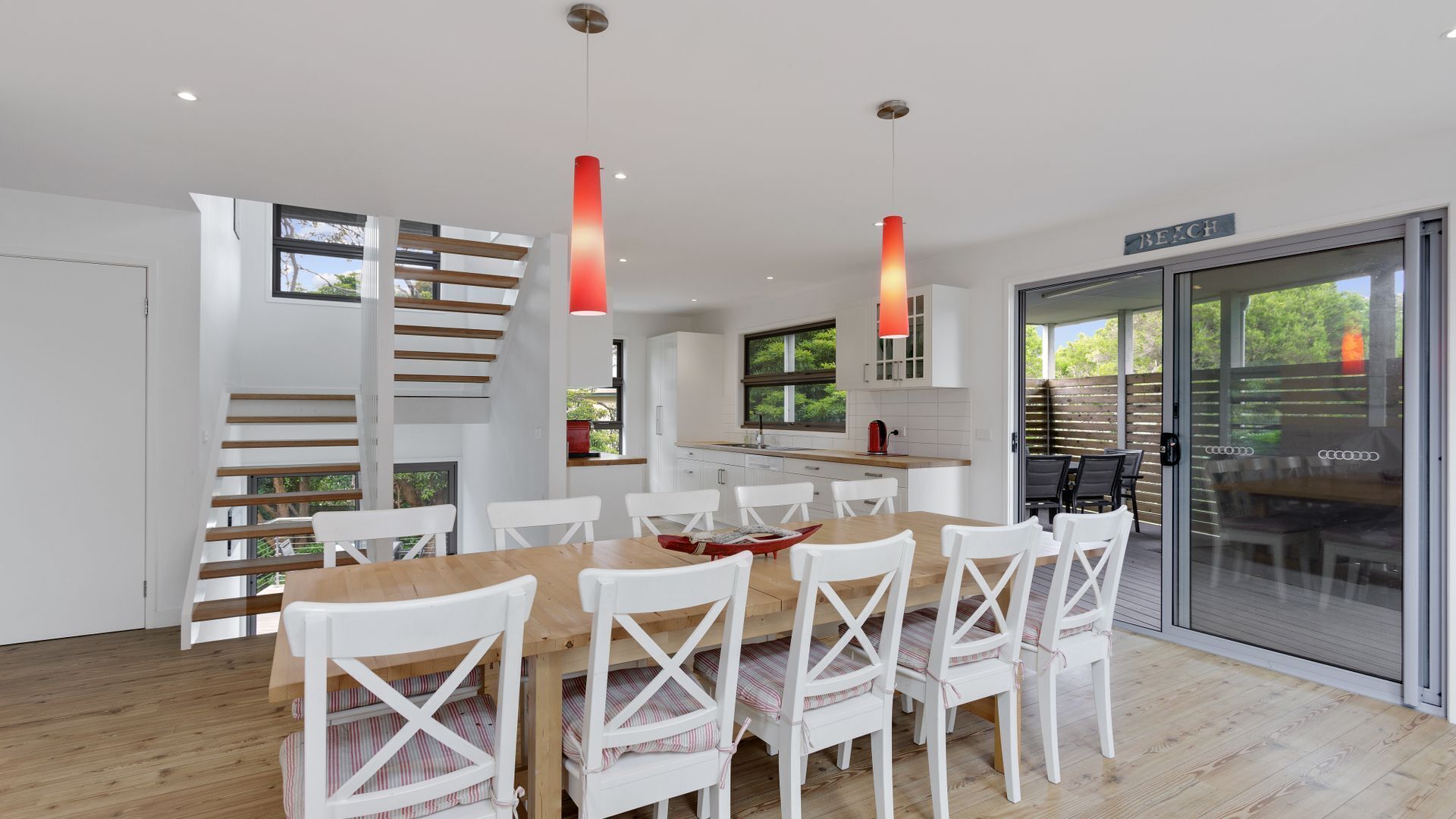 Une cuisine moderne avec des meubles blancs, une table à manger en bois et des chaises blanches, ainsi que des luminaires suspendus.