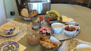 Una tavola imbandita per la colazione con pane, dolci, frutta e una caffettiera.