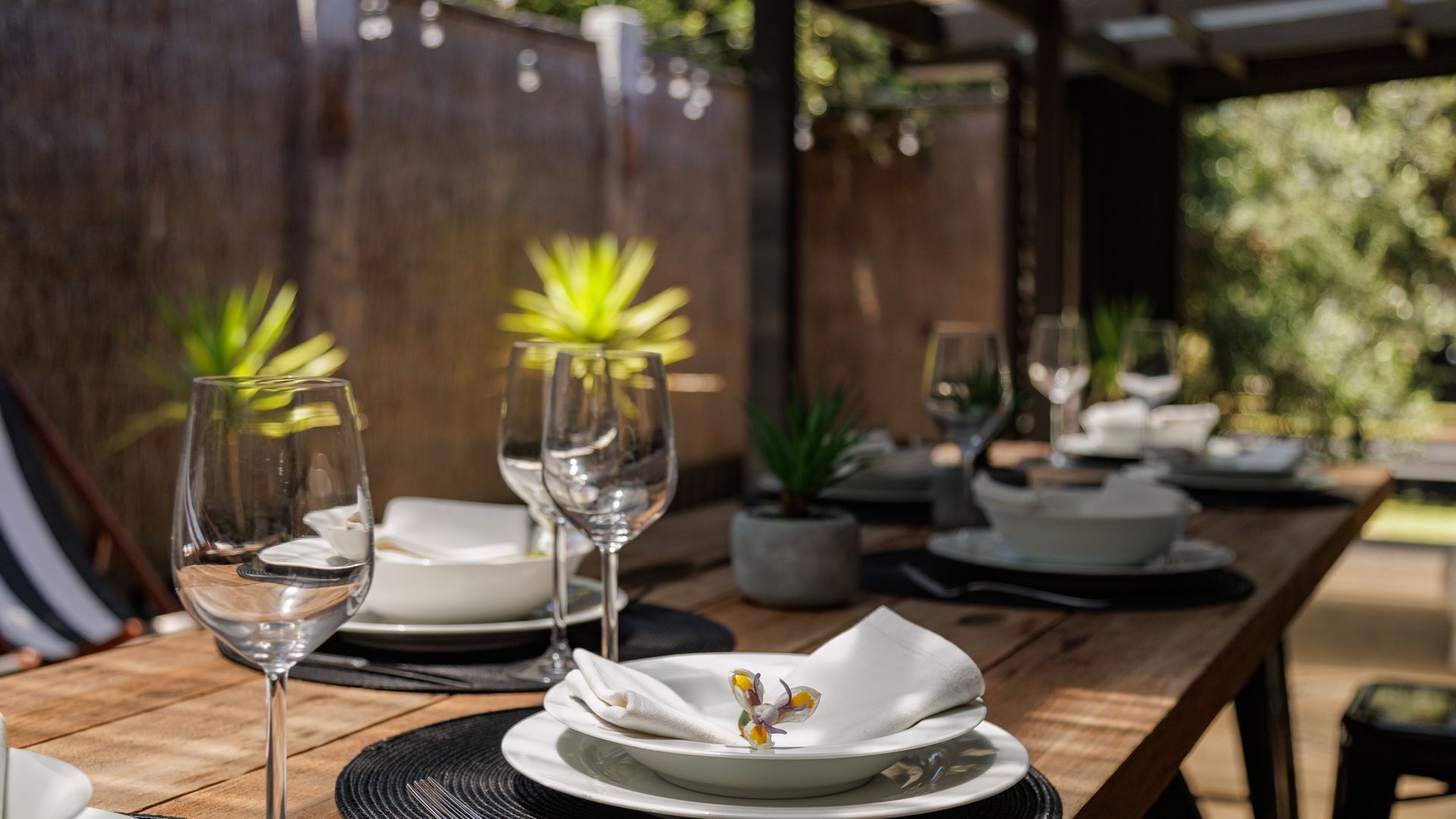 A wooden table set for dining with clear glassware and white plates.