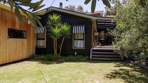 A modern house with a wooden exterior, two windows with striped awnings, a small patio, and a grassy yard.