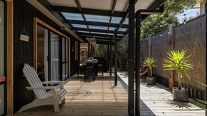 A covered patio with a wooden deck, a table with chairs, and potted plants.