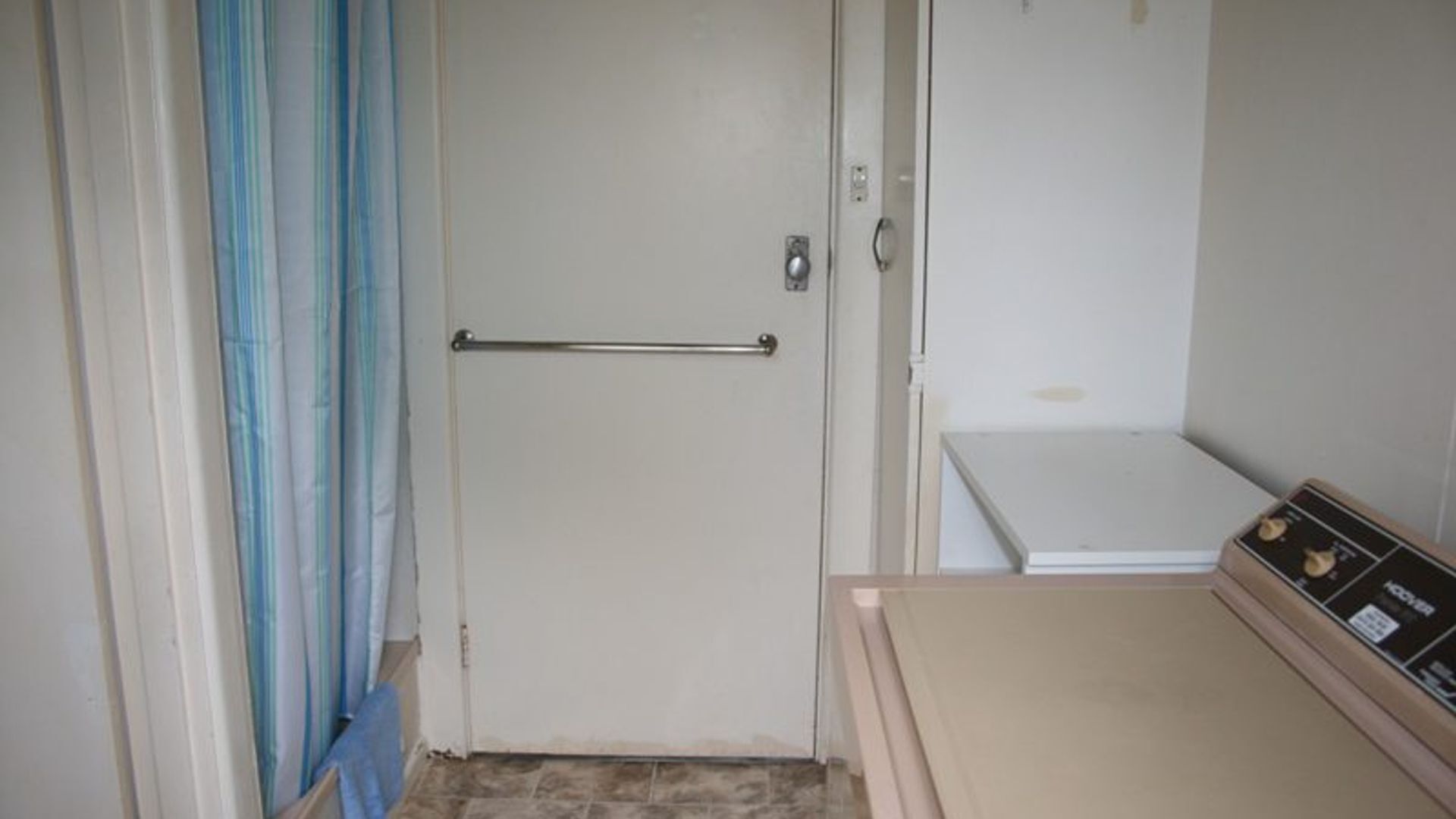 Um espaço pequeno e fechado, com porta, puxador de metal e suporte para toalhas.