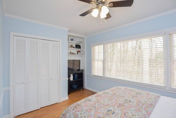 A bedroom with a bed, a closet, a shelf unit, and a window with blinds.