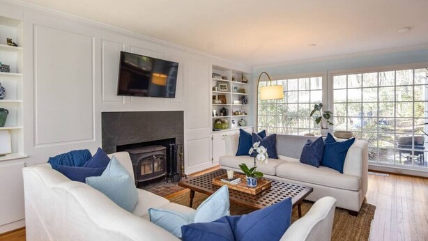 Una sala de estar con chimenea, sofás blancos y un televisor.