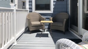 Relax on the porch with two comfortable chairs and a table, surrounded by a white railing and a window offering a view of the street.