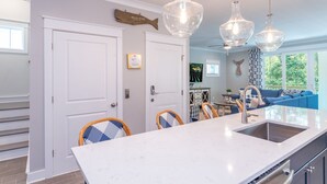 Una cucina moderna con un'isola grande, mobili bianchi e illuminazione a sospensione.
