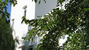 Un edificio blanco con un ventanal grande y una puerta, rodeado de follaje.