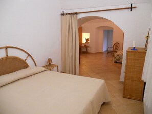 A bedroom with a bed, a nightstand, a dresser, and an arched doorway leading to a dining area.