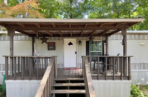 A wooden deck with a covered porch leading to a door, surrounded by a wooden fence and trees.
