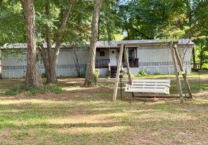 A rustic wooden structure with a porch and a swing set in a wooded area.