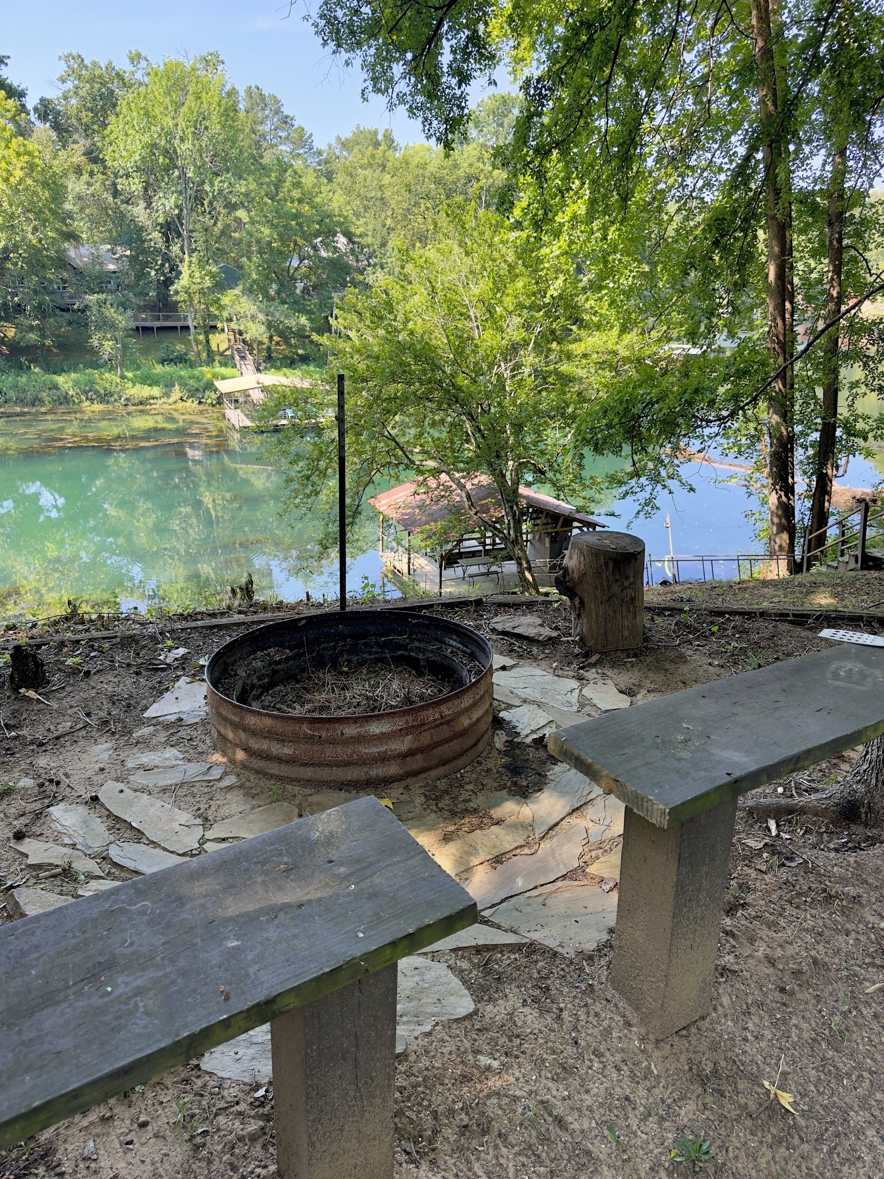 A lakeside park with a fire pit, benches, and a wooden structure.