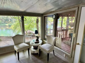 A room with two chairs, a small table, and a view of a lake through large windows.