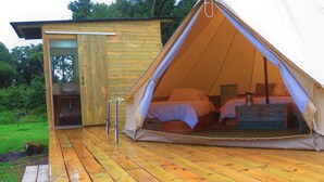 Una terraza de madera que lleva a una carpa con dos camas y un baño pequeño.