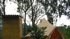 Una carpa y una estructura de madera en una zona con césped, con árboles al fondo.