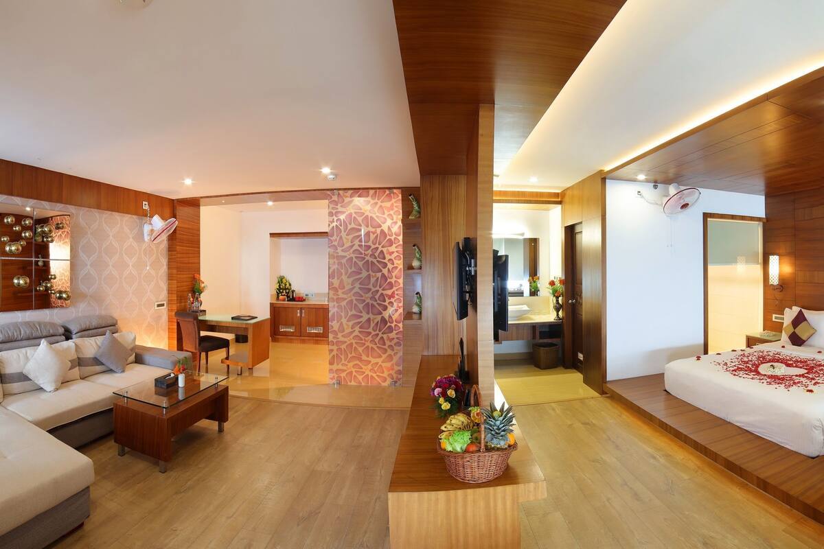 A modern hotel room with a large bed, a sitting area with a sofa and coffee table, a bathroom with a bathtub, and a dining area.