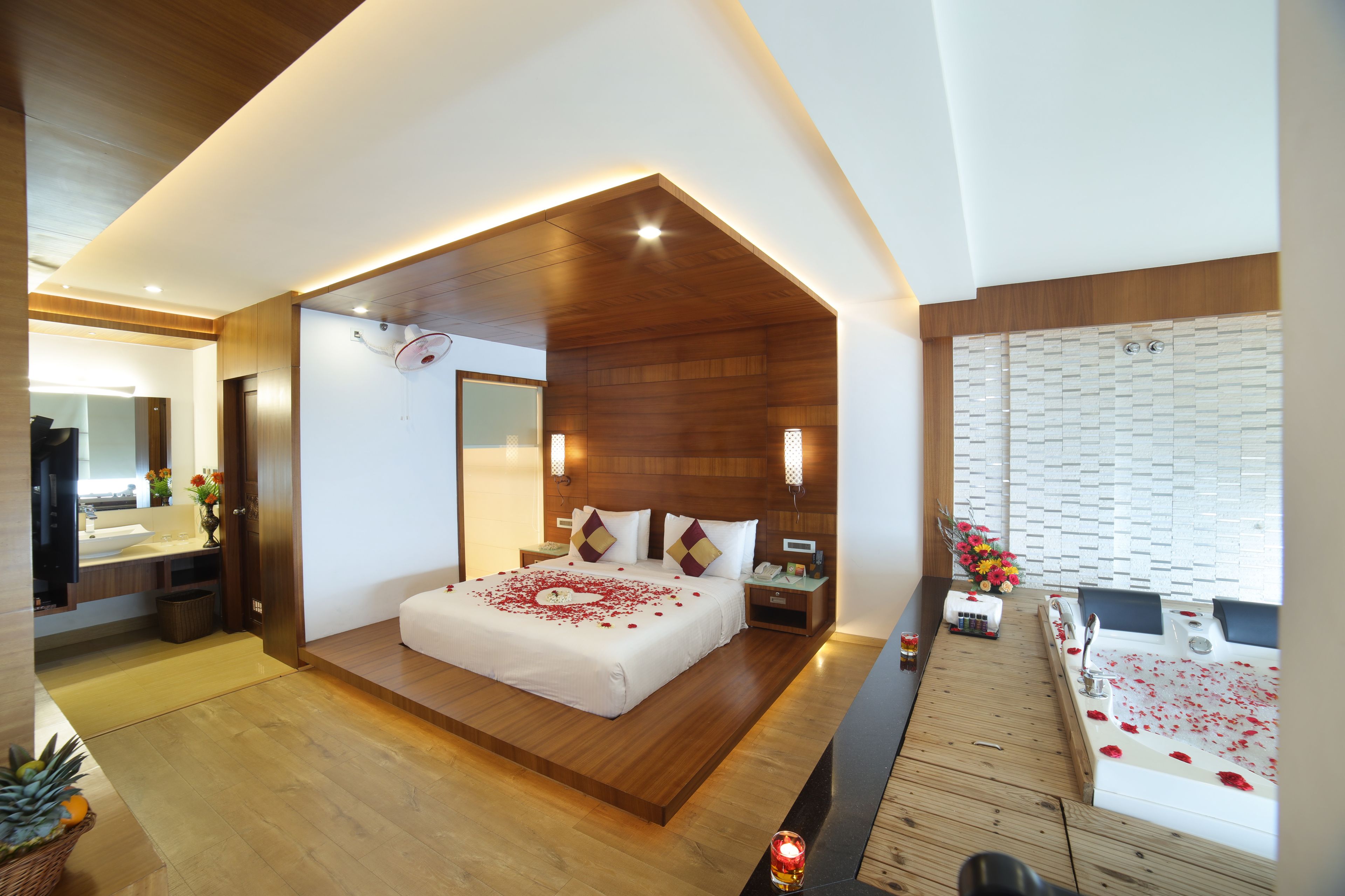 Una habitación de hotel moderna con techo de madera, una cama grande con pétalos de rosa, una bañera con pétalos de rosa y suelo de madera.