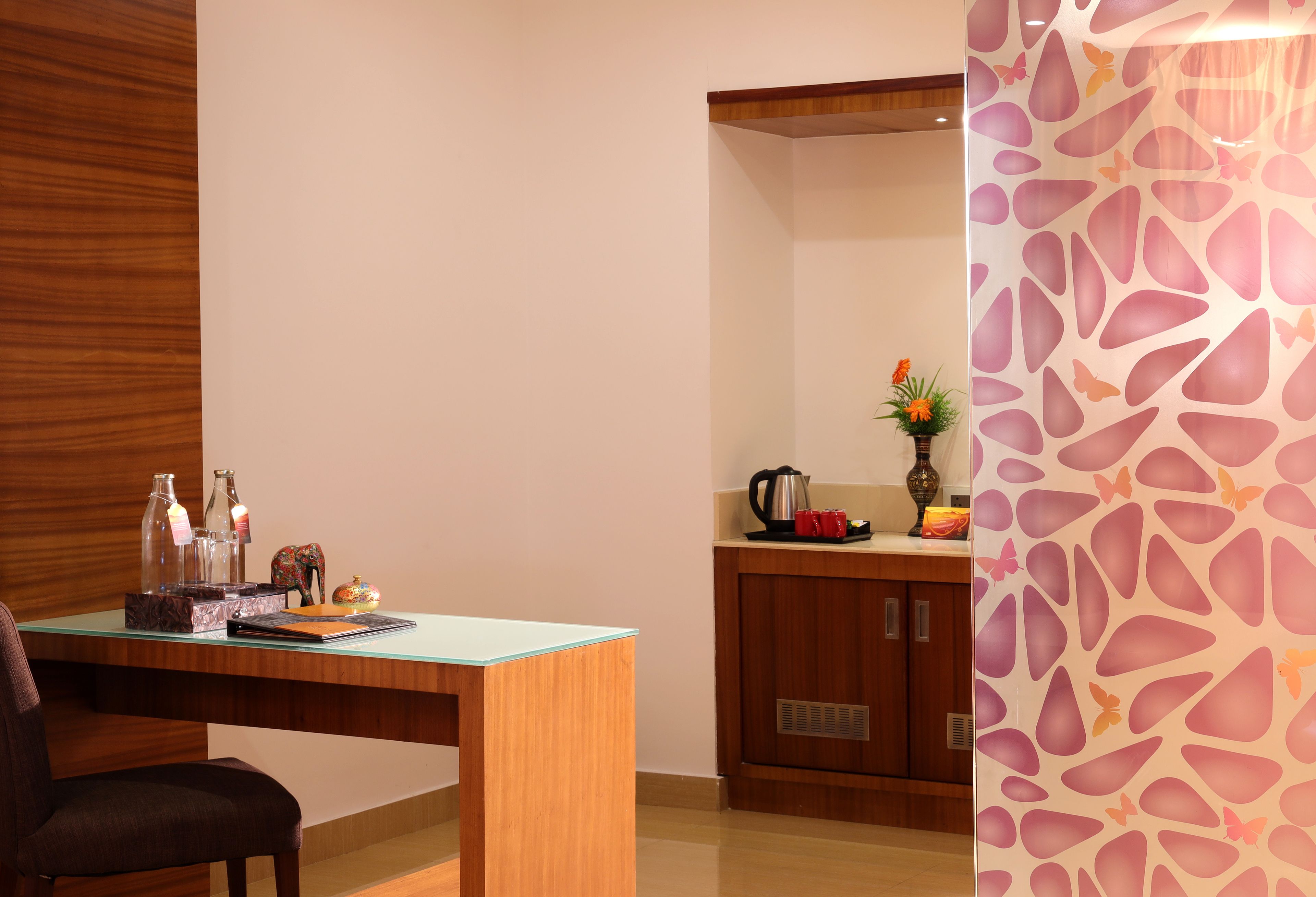 Une cuisine moderne avec des meubles en bois, une table à plateau en verre et un mur décoratif orné d’un motif de feuilles.