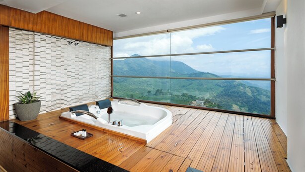 Un baño moderno con una bañera grande, suelo de madera y vistas a la montaña a través de un amplio ventanal.