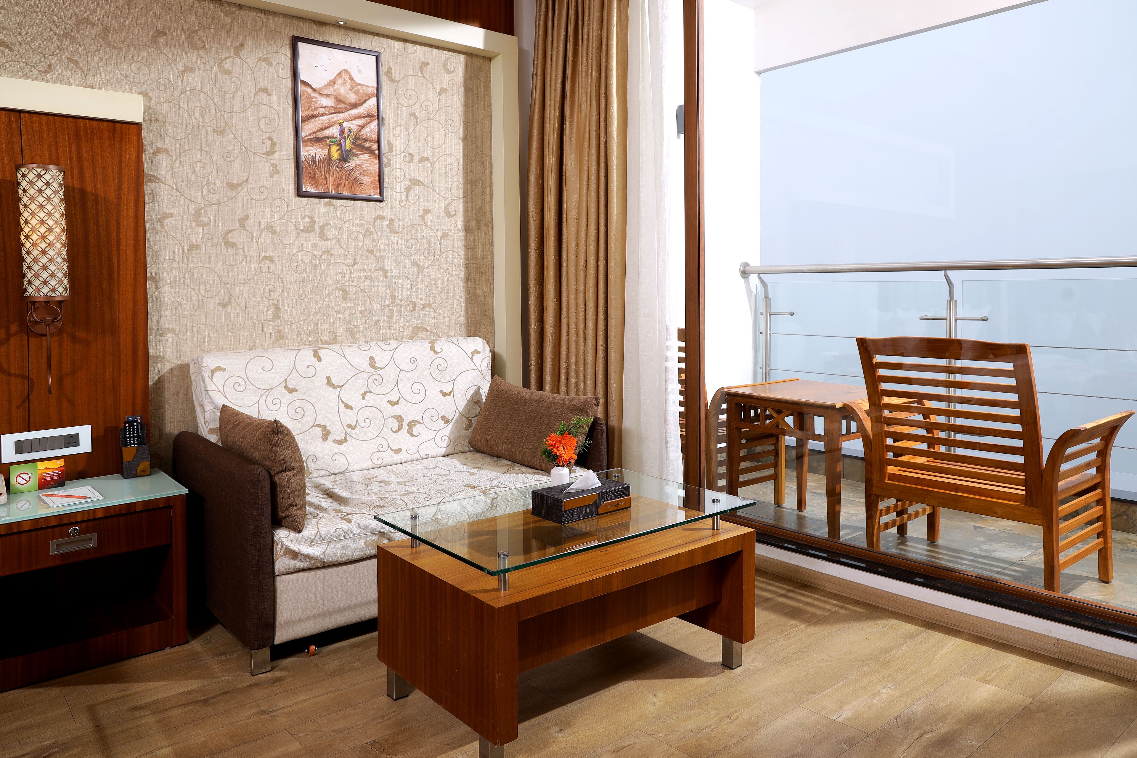 A modern living room with a sofa, a glass coffee table, a wooden desk, and a balcony with a table and chairs.