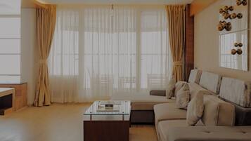 A modern living room with a glass coffee table, a sofa, and a large window with sheer curtains.