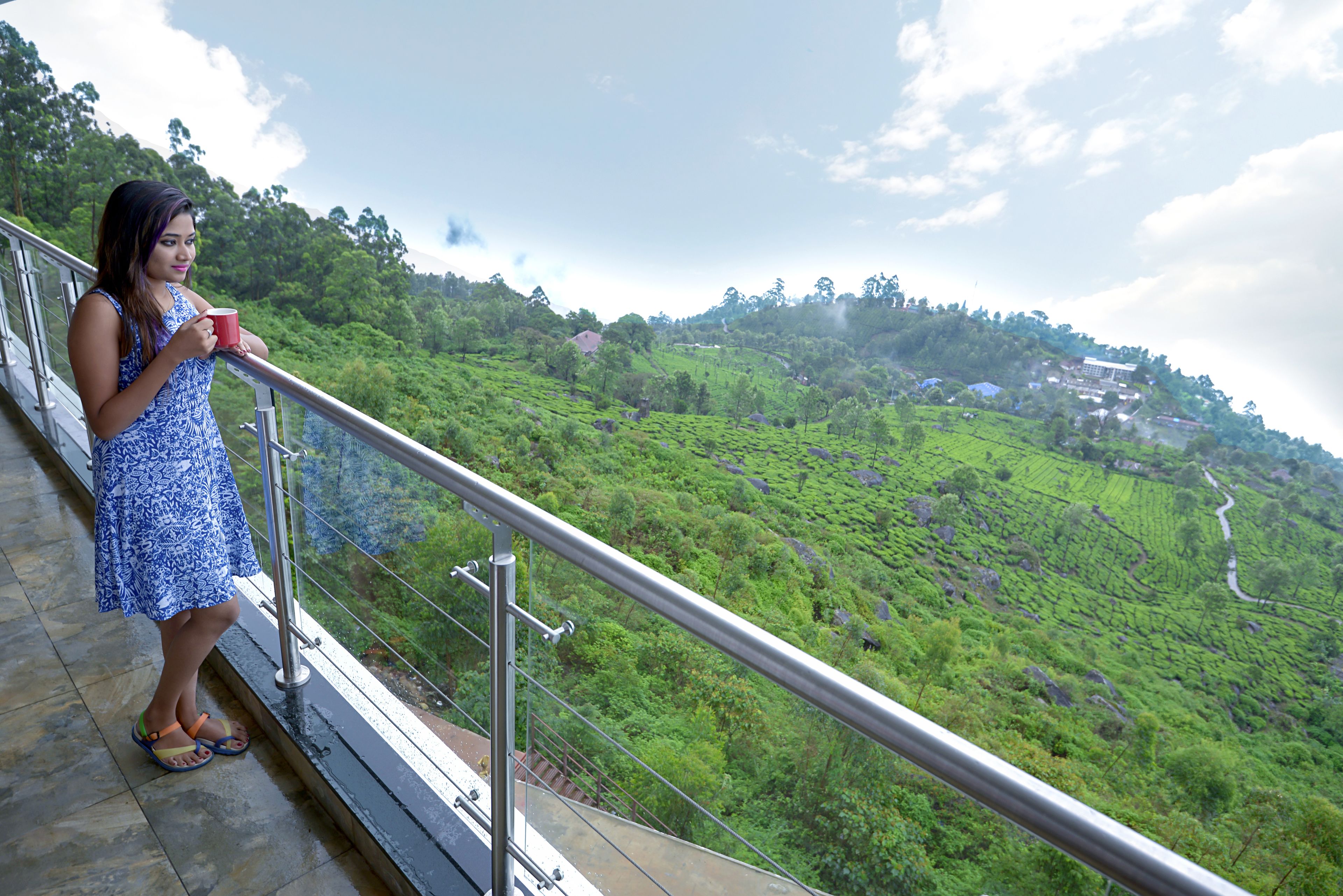 A person standing on a balcony with a view of a green landscape.