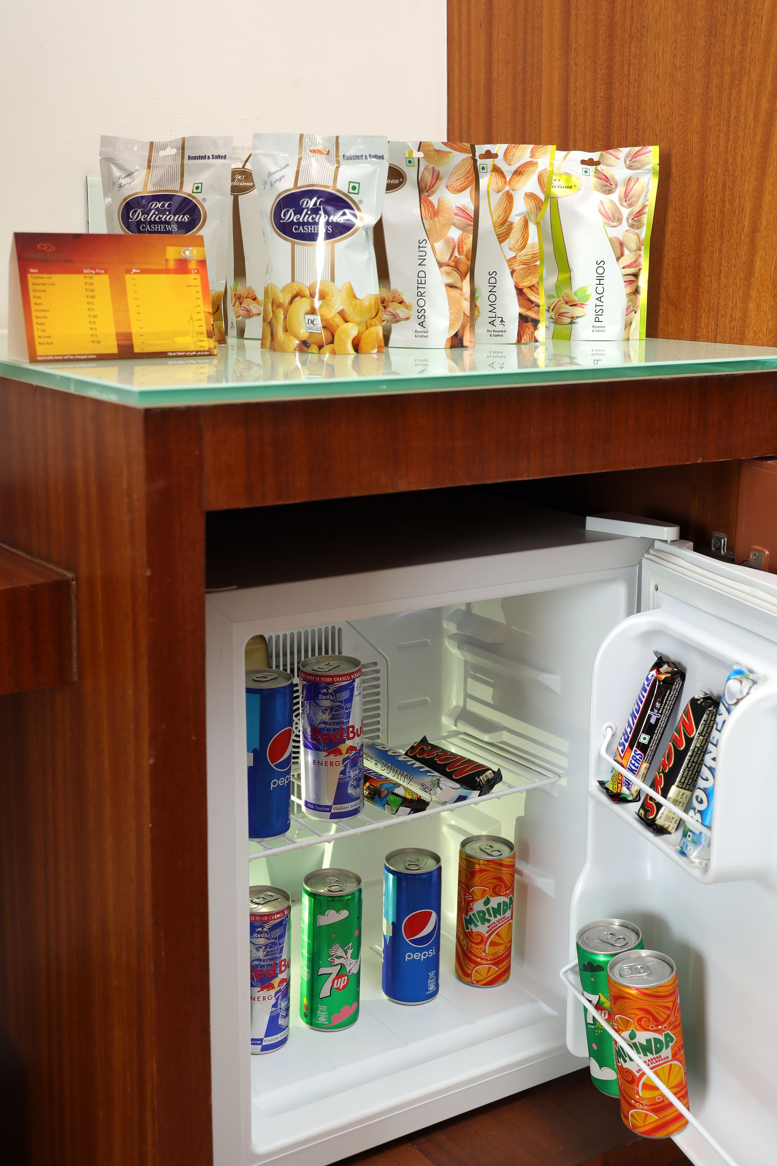 A mini-fridge stocked with various beverages and snacks, including cans of soda and packaged nuts.