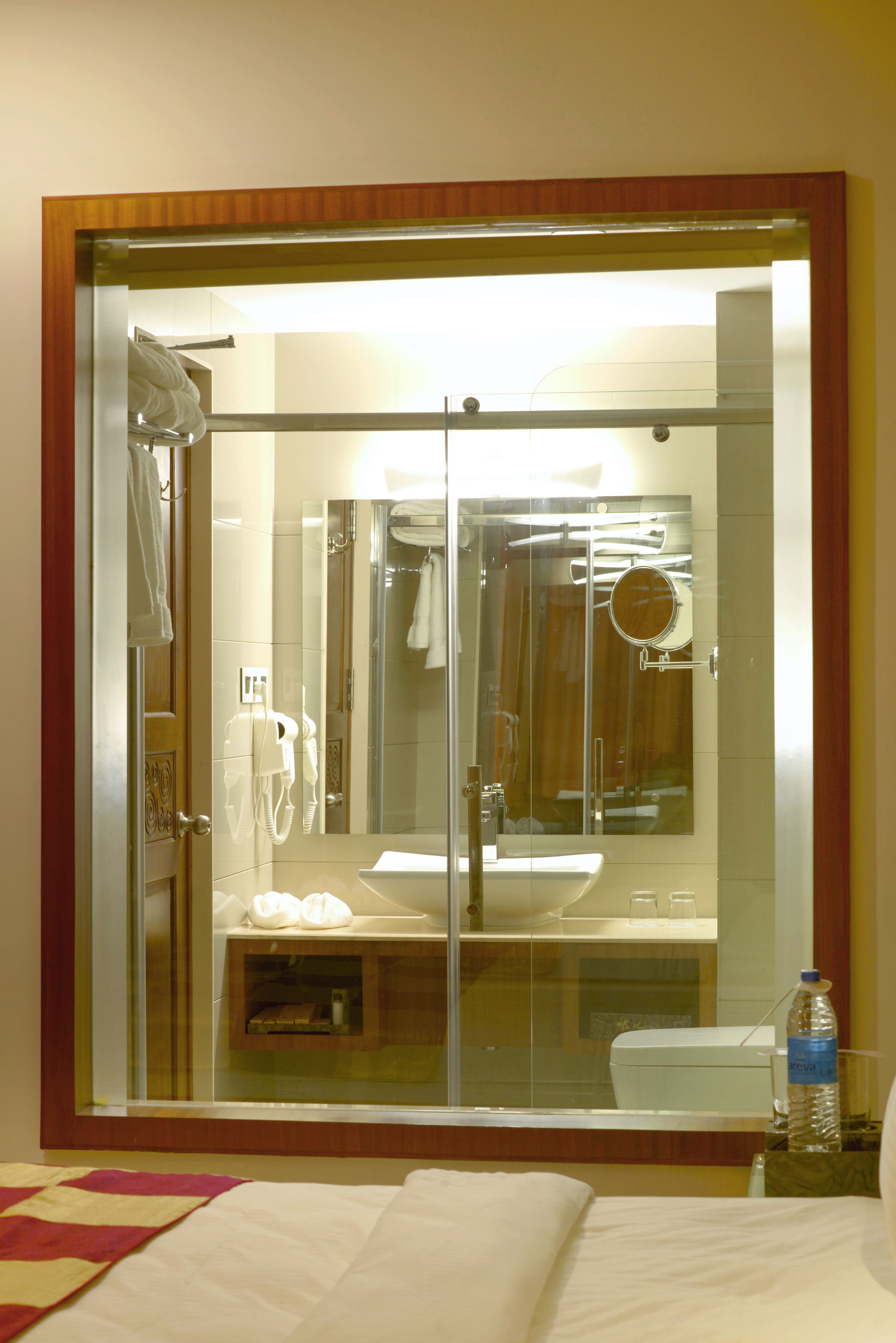 Baño de hotel con ducha de vidrio, lavamanos, espejo y toallero.