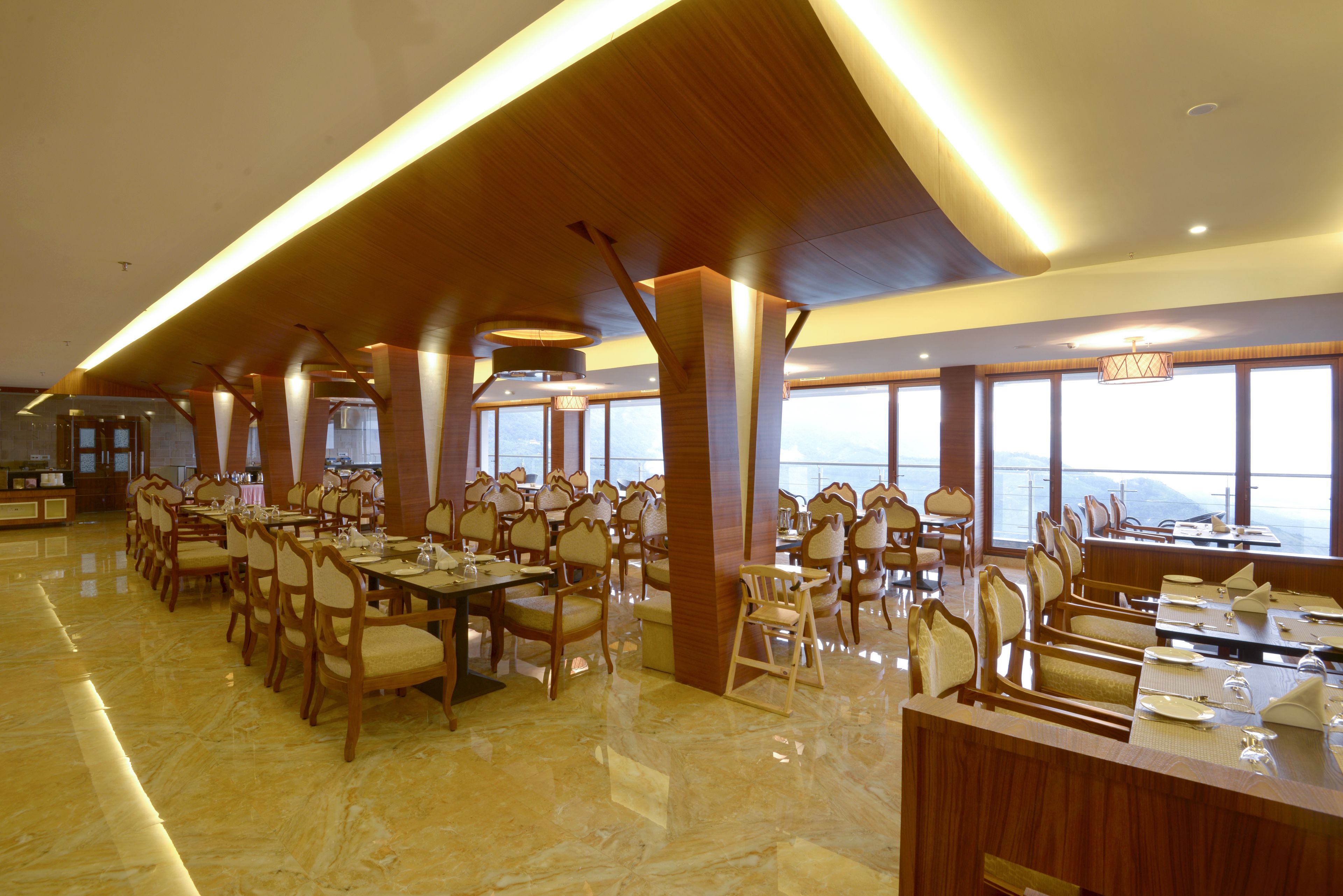 A spacious dining area with multiple tables and chairs, large windows offering a view, and a polished marble floor.