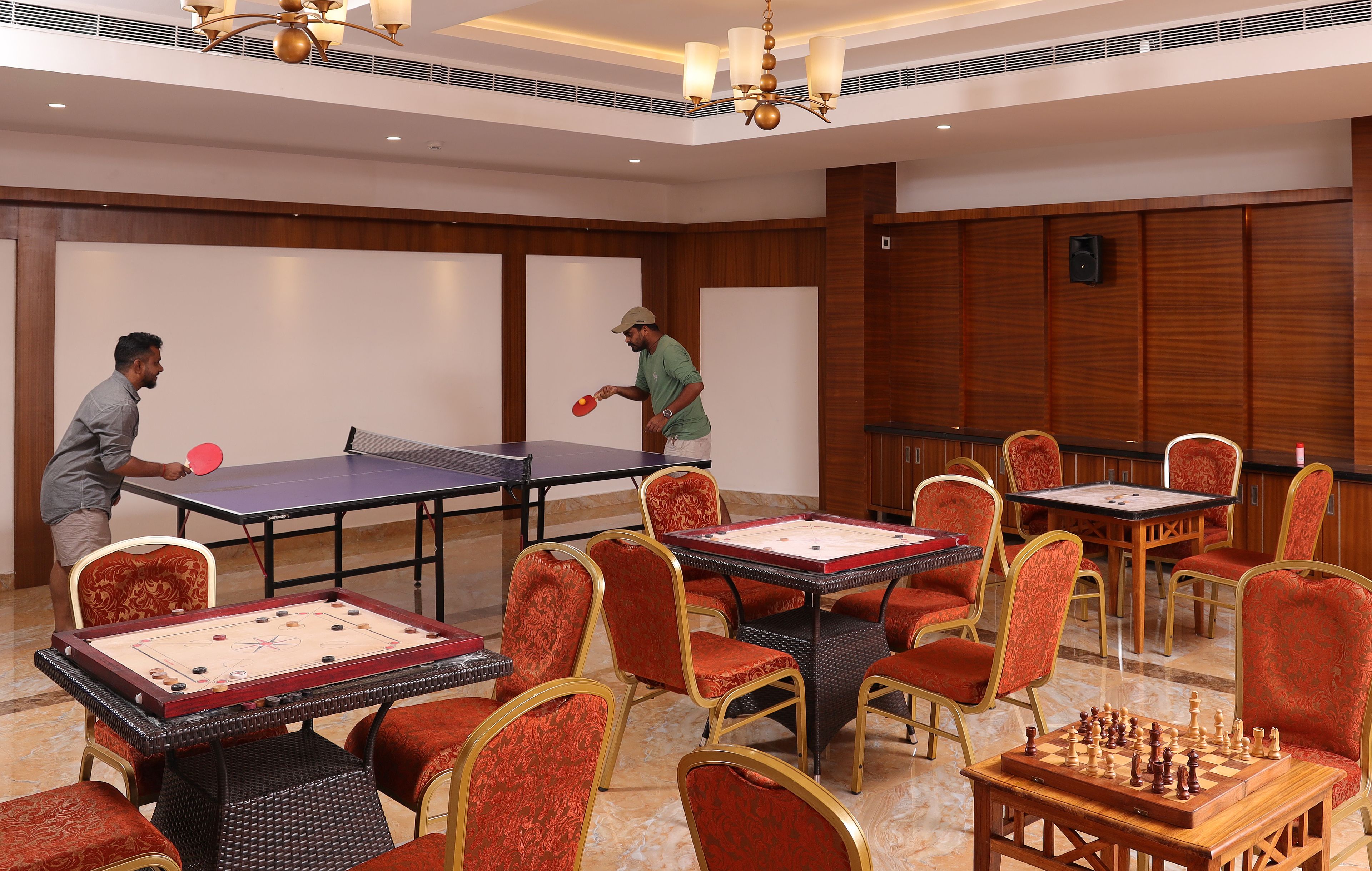 A room with ping pong tables and chess tables, furnished with red upholstered chairs.