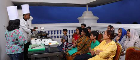 A chef preparing food in a kitchen with a group of people seated in the background.