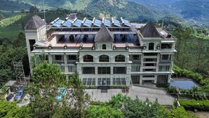 Un edificio grande con varios pisos, paneles solares en el techo y vistas a colinas verdes al fondo.