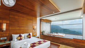 Una habitación de hotel moderna con una cama grande, paneles de madera, un ventanal con vistas a la montaña, un baño pequeño y suelo de madera.