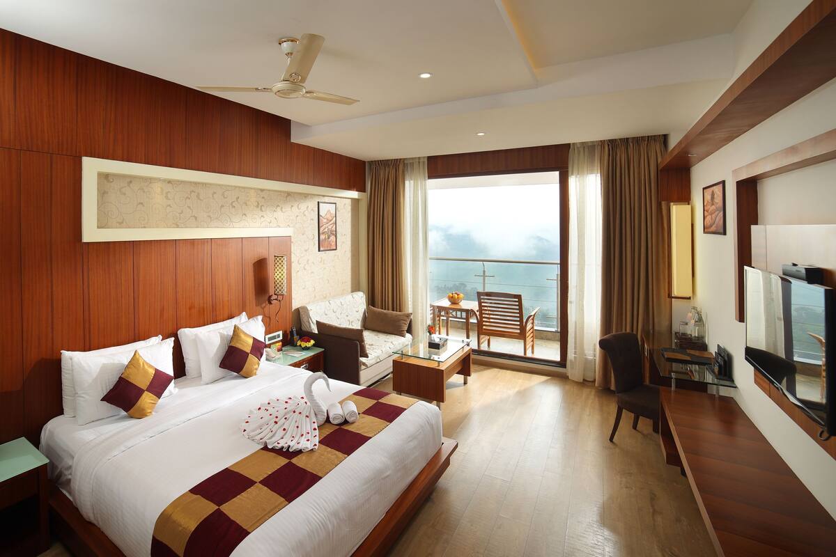 A hotel room with a large bed, a desk, a chair, a television, and a balcony with a view.