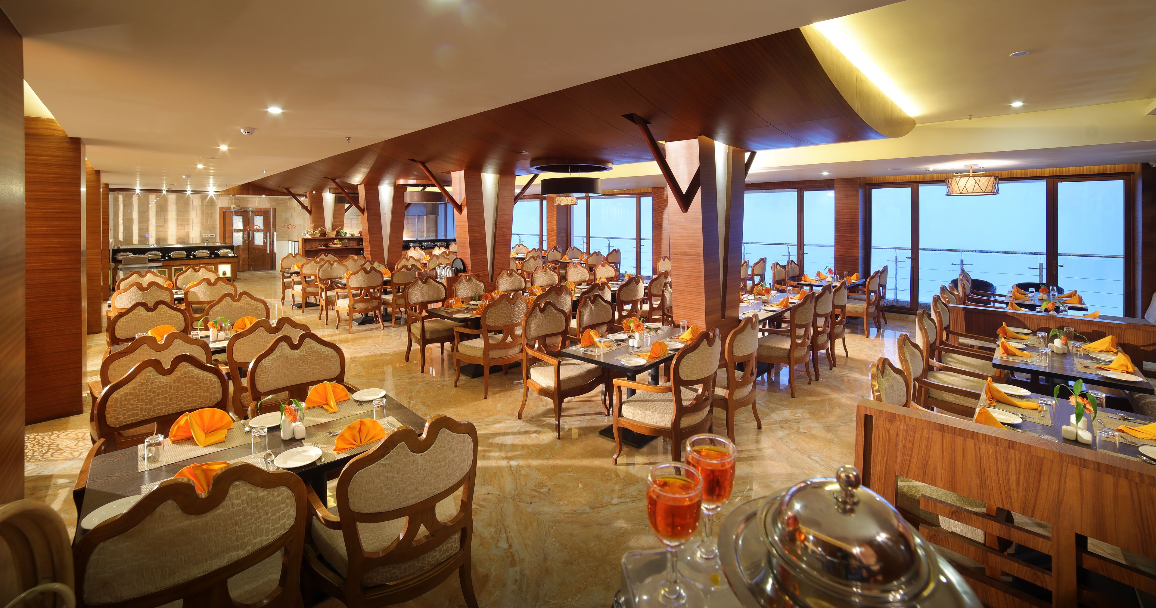 A spacious dining area with multiple tables and chairs, large windows offering a view of the sea, and a modern interior design.