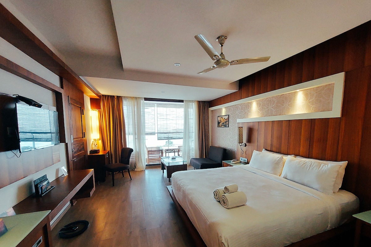 Habitación de hotel con cama, escritorio, silla, televisión, ventilador de techo y vistas al exterior.