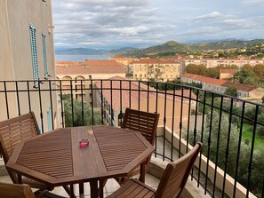 A balcony with a wooden table and chairs, overlooking a town with red-roofed buildings and green hills. - Apartment/ flat - Ile Rousse (Ile Rousse)