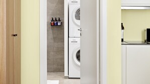 Une buanderie équipée d’un lave-linge et d’un sèche-linge, d’une armoire en bois et d’un coin cuisine avec un plan de travail et des placards.