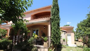 Una casa a due piani con un balcone, immersa nel verde e con un albero alto.