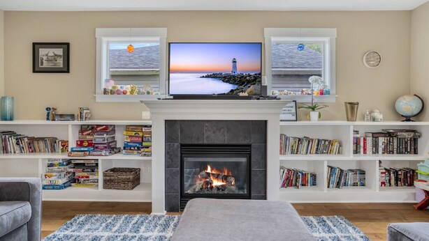 A living room with a fireplace, a television mounted above it, and bookshelves filled with books. - Spacious Family Friendly SE, Free Parking, A/C, Walk to food, Toy Room, Crib! (Portland)