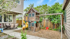 A backyard with a wooden playhouse, a slide, and a swing set. - Spacious Family Friendly SE, Free Parking, A/C, Walk to food, Toy Room, Crib! (Portland)