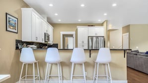 A modern kitchen with white cabinets, a stainless steel refrigerator, and four white bar stools. - Spacious Family Friendly SE, Free Parking, A/C, Walk to food, Toy Room, Crib! (Portland)