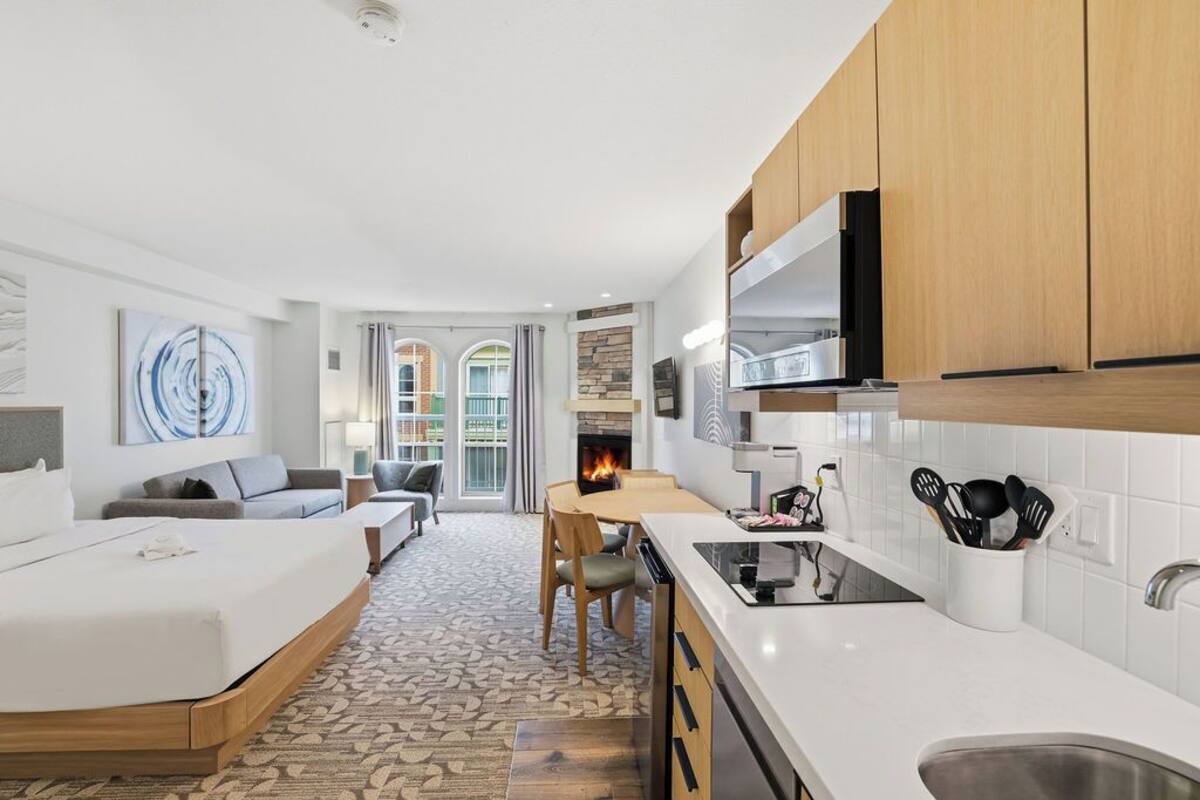 Une chambre d’hôtel moderne comprenant un lit, un coin repas avec une cheminée, une kitchenette et une vue sur une cour intérieure.