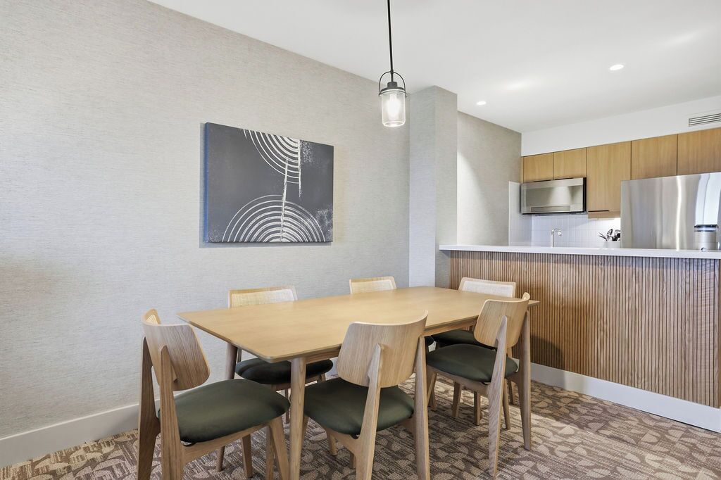 A dining area with a wooden table and chairs, a modern kitchen with stainless steel appliances, and a wall-mounted artwork.