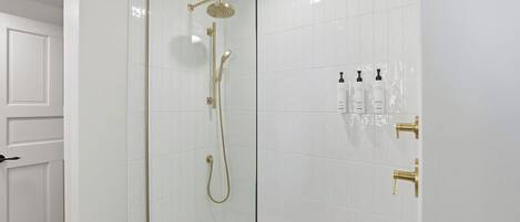 Casa de banho moderna com cabine de duche em vidro, paredes revestidas de azulejos brancos e porta branca.