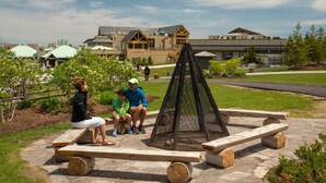 A stone bench area with a fire pit in the center, surrounded by greenery and a building in the background. - Blue Mountain Resort Mosaic Suites (The Blue Mountains)